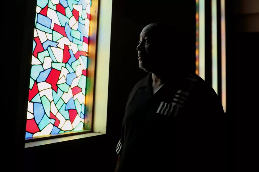 Dramatic profile photo of man in the dark staring out a colorful stained glass window